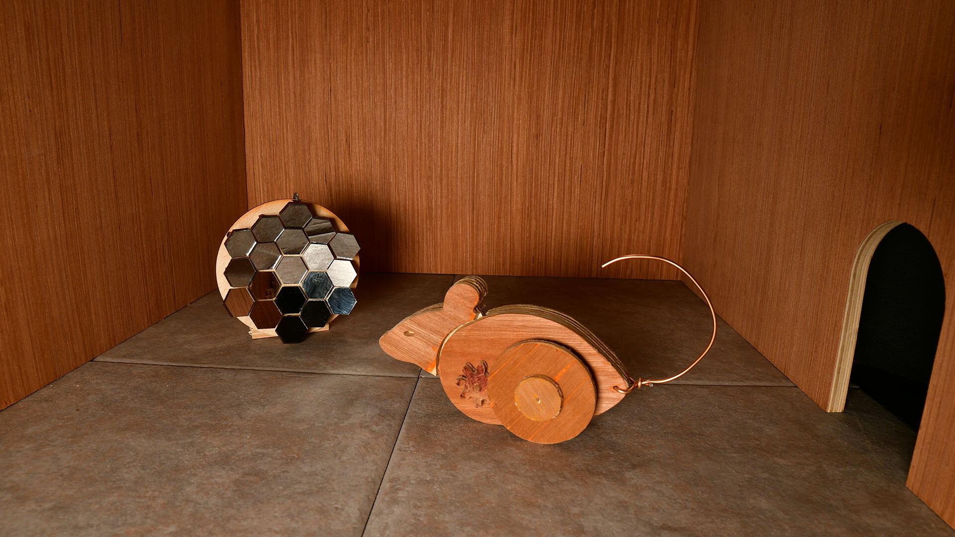 Wooden mechanical mouse on tile examining disco ball like array in Ealu