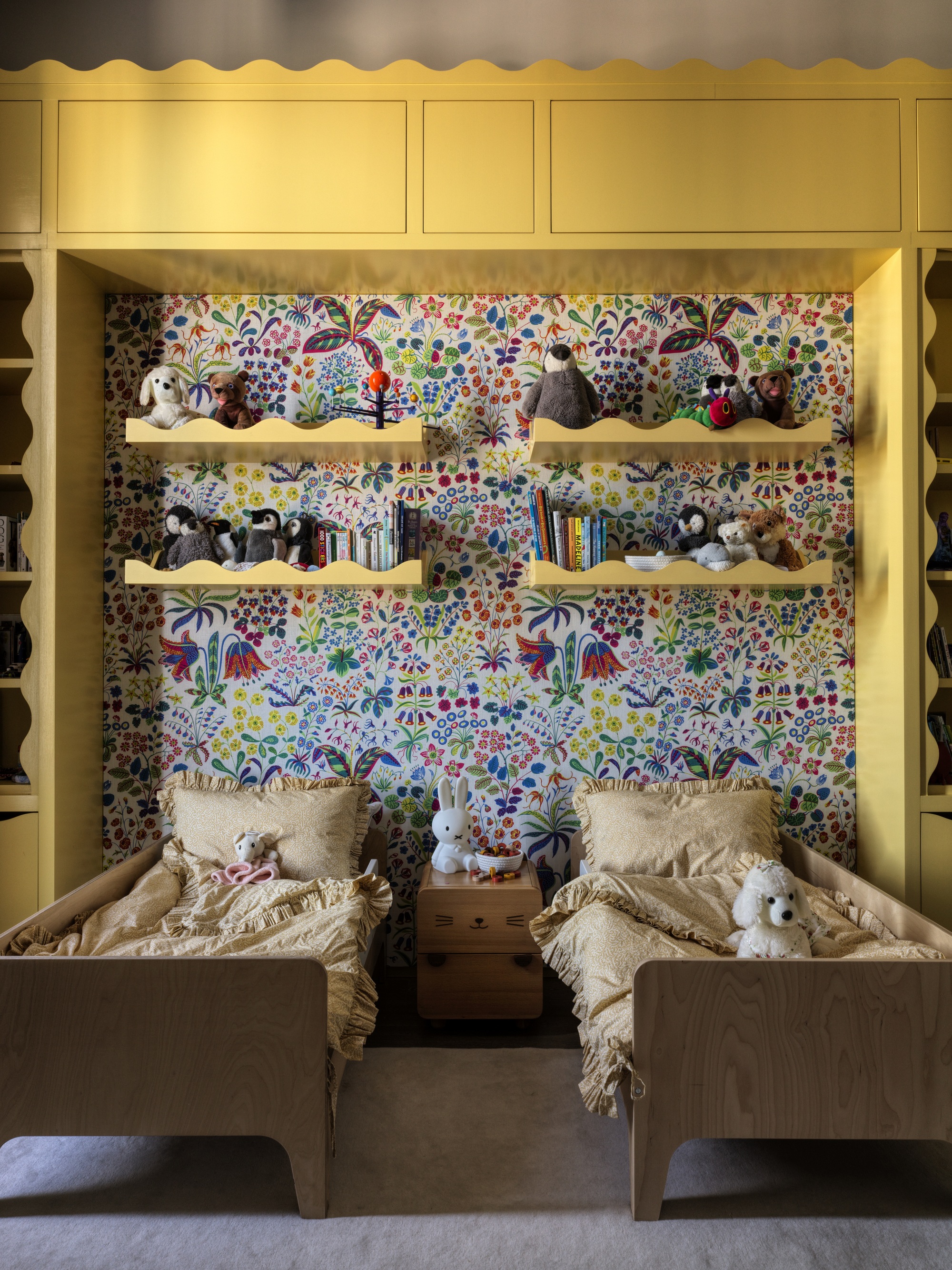 kids bedroom with yellow built-in cabinetry with scalloped edges, floral wallpaper, floating scallop shelves with toys and books, and two timber twin beds with yellow sheets