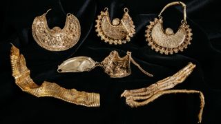 Intricate golden jewelry is displayed on black velvet.