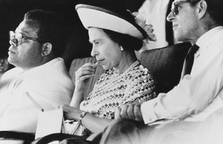 Queen Elizabeth II applies her lipstick at a function during a visit to Fiji with Prince Philip (right), February 1977