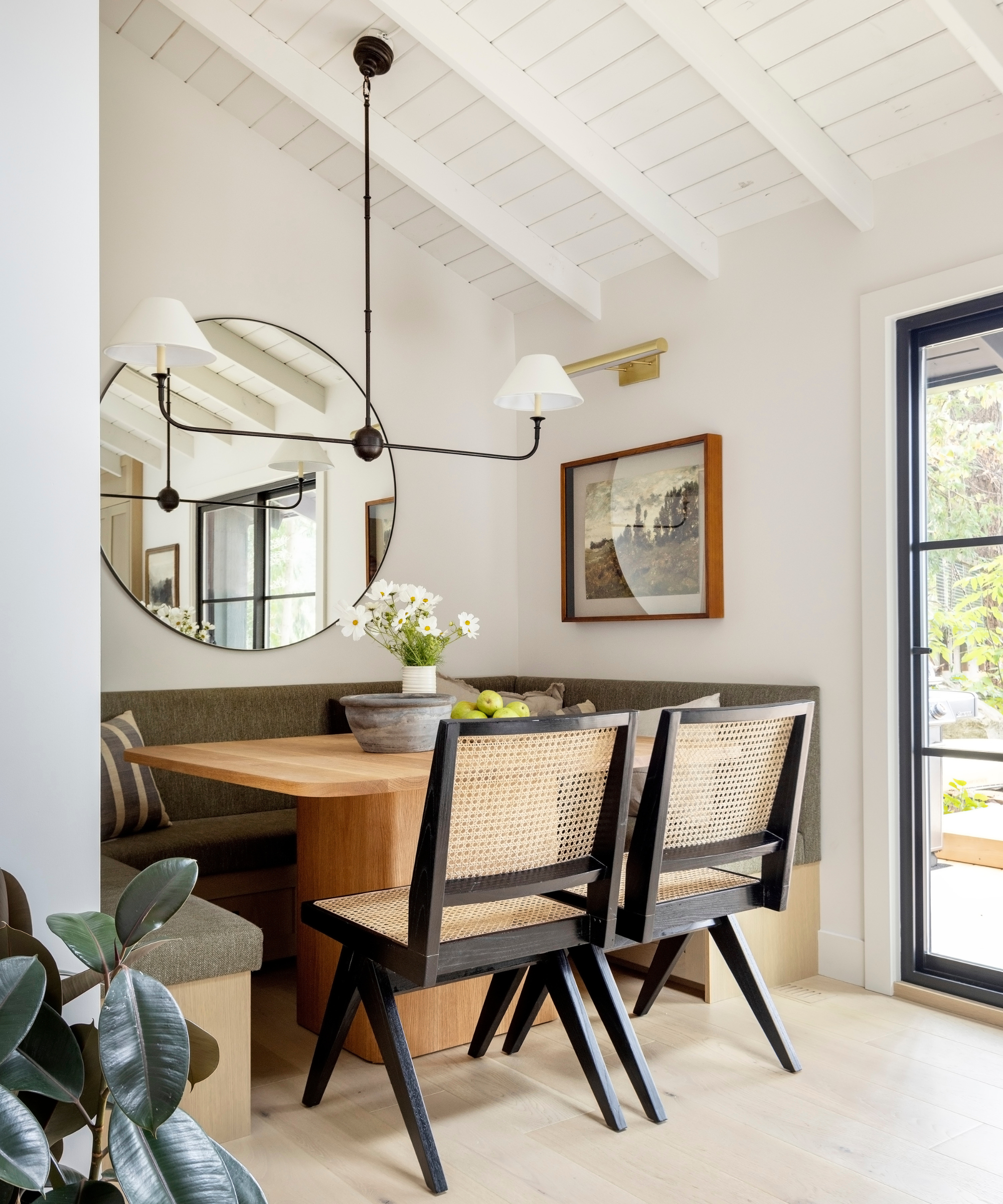 A neutral kitchen nook with a wooden dining table, olive green bench, and lofted white ceilings