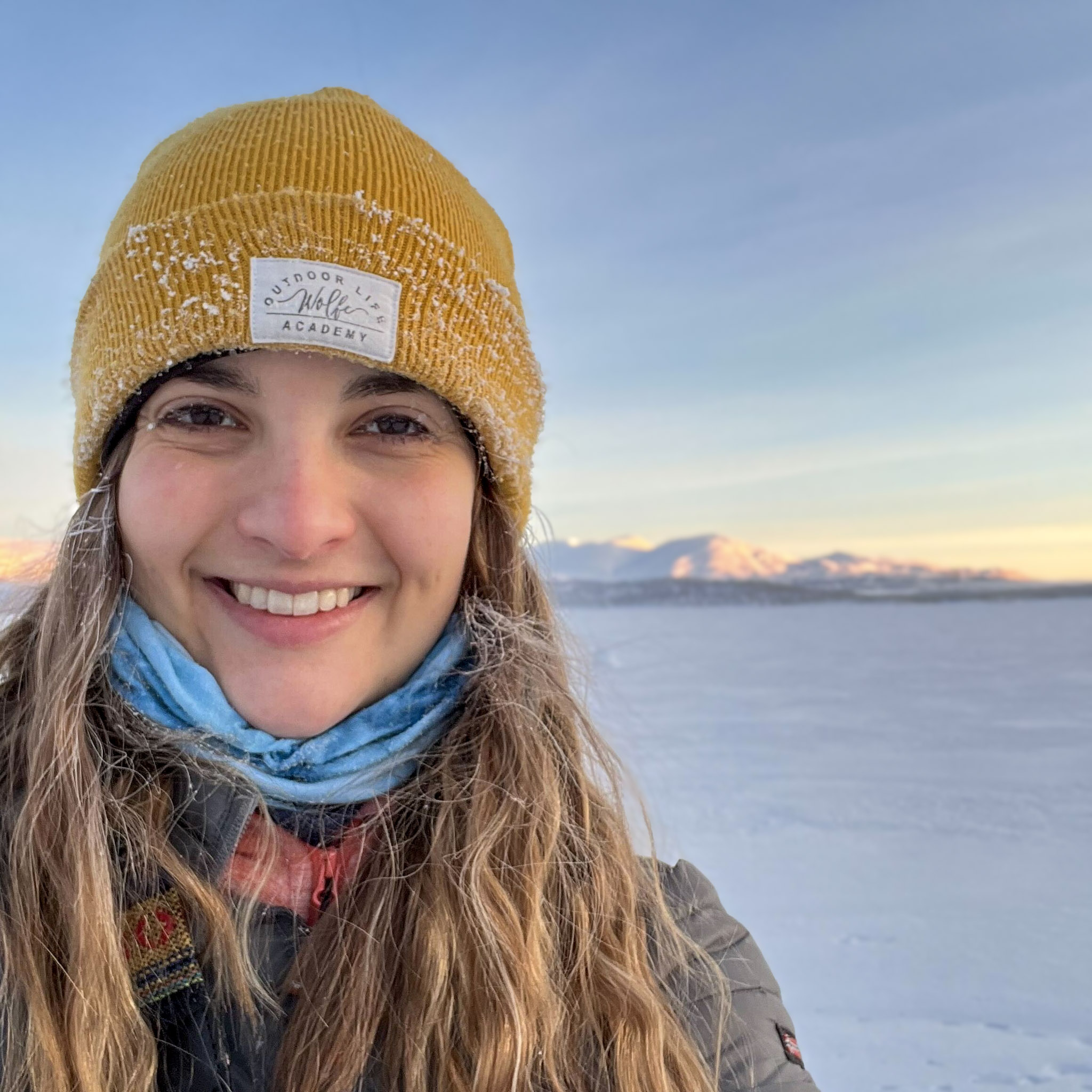 a woman wearing a yellow hat smiles under the blue light of the polar night. 