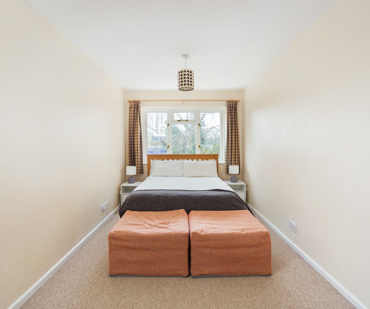 A narrow bedroom with two cushions at the end of the bed and two side tables