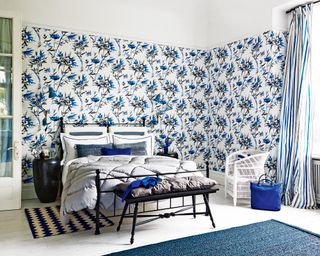 A bedroom with black, white and blue patterned wallpaper, white floorboards, blue and white striped drapes and monochrome accents.