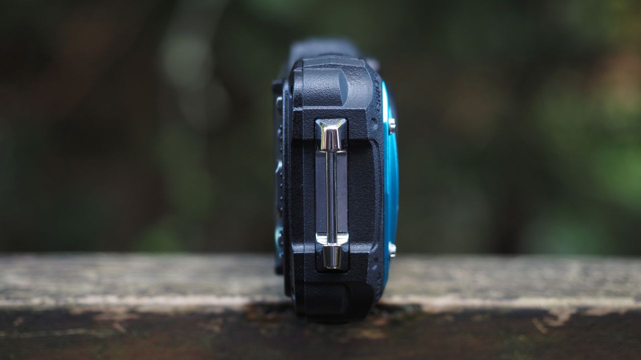 Close up of a Pentax WG-90 sitting on a wooden surface in front of woodland