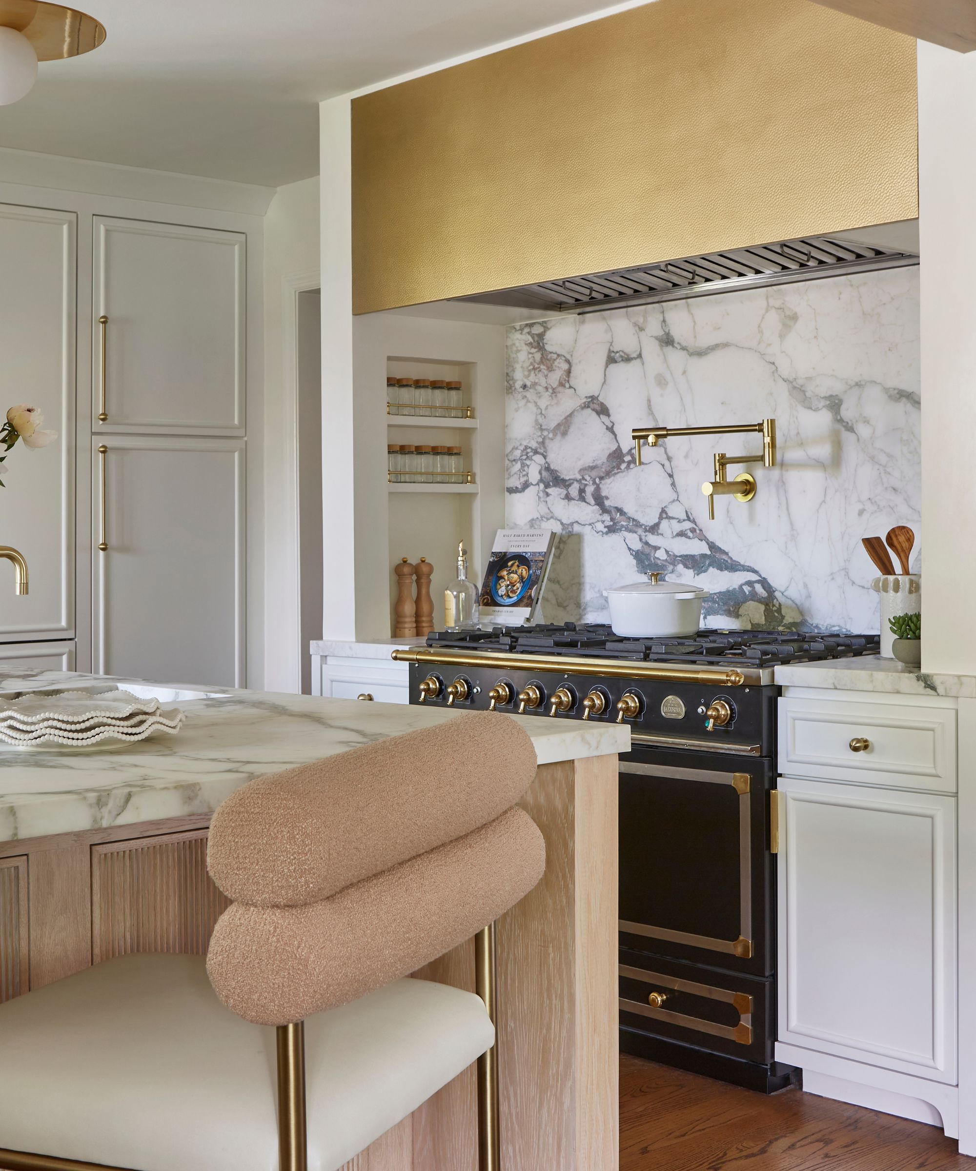 a white kitchen with a black range cooker and a brass hood with recessed niche storage