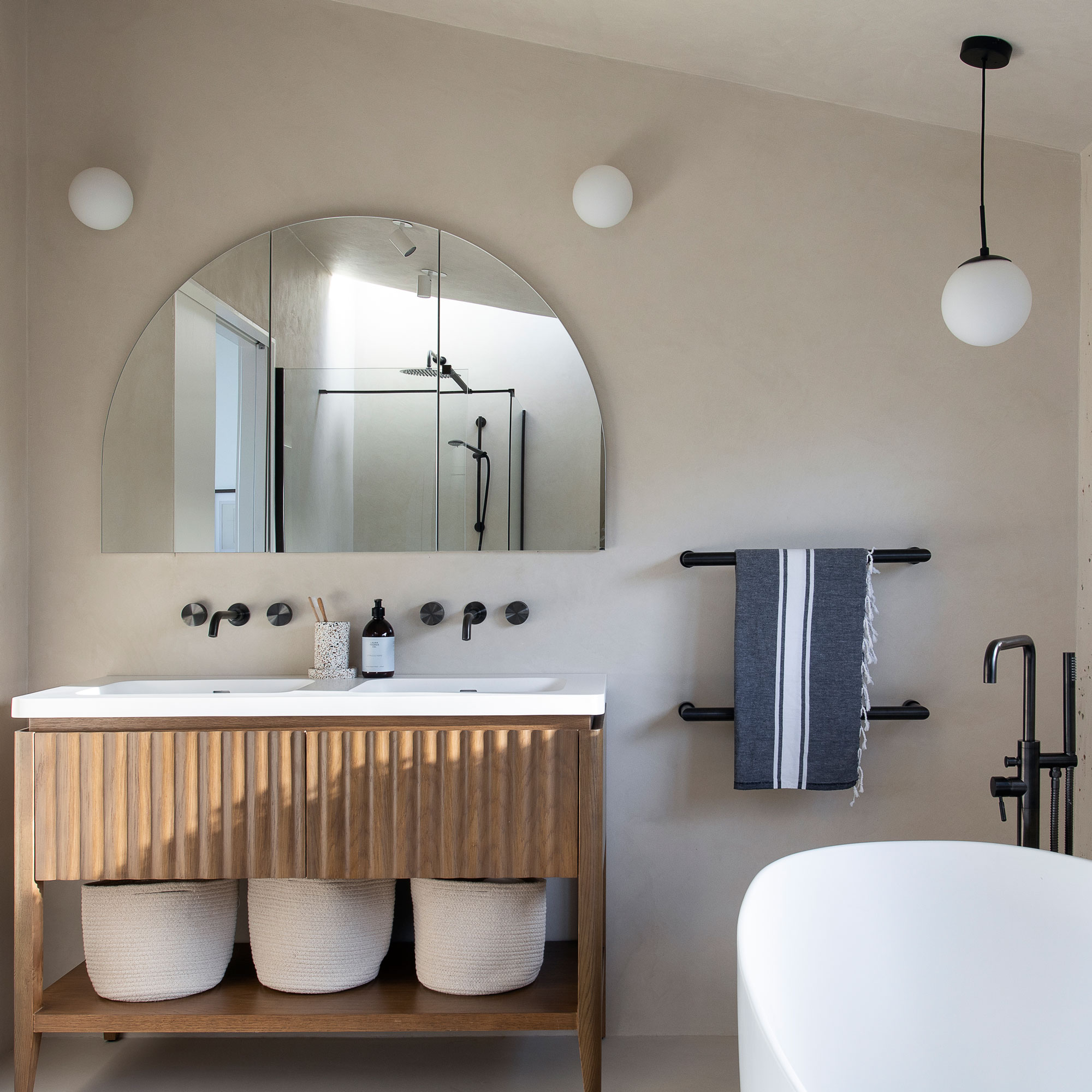 Plaster bathroom with arch mirror, wooden vanity and white tub