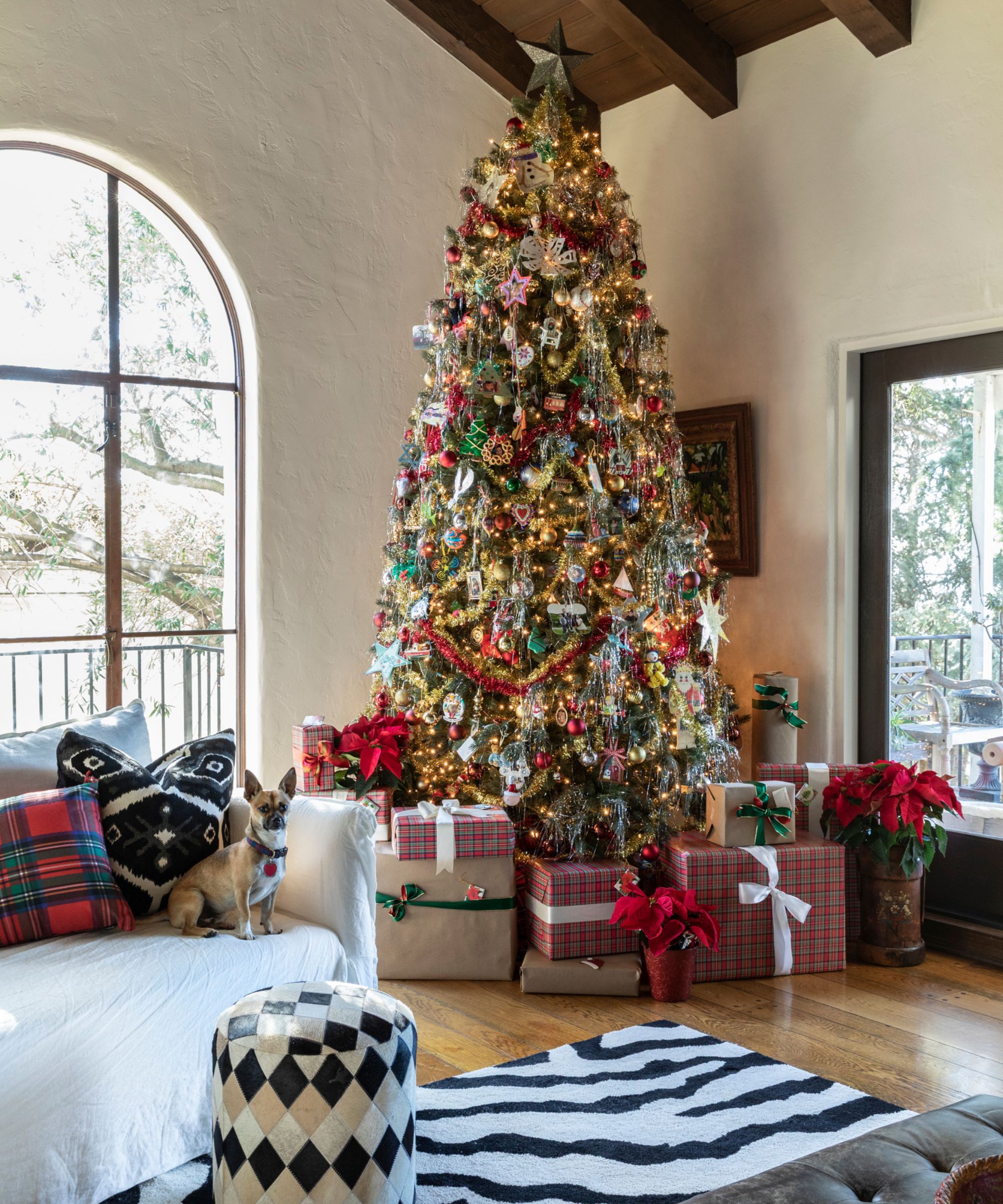 a neutral living room with wooden ceiling styled for christmas with a large christmas tree decorated with lots and lots of ornaments and garlands with plaid wrapped gifts