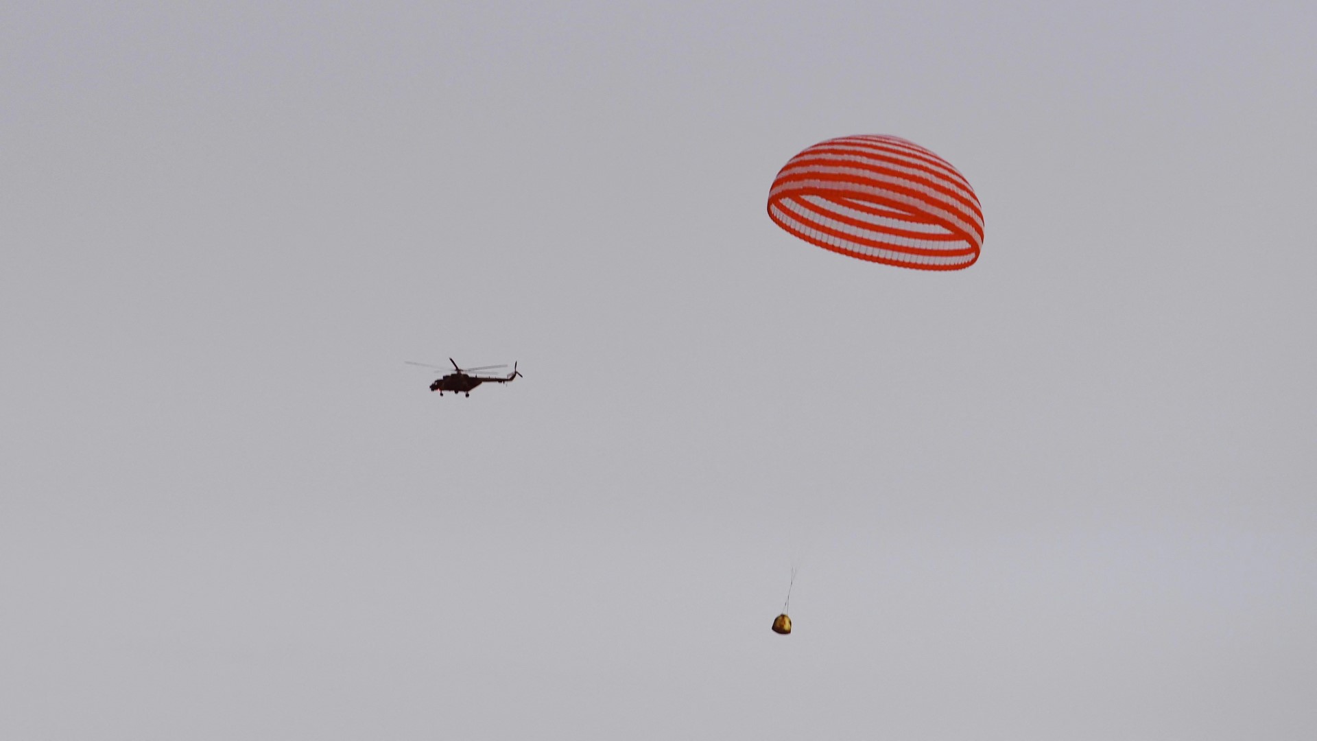 Chinese Shenzhou 15 space capsule descending under parachute with recovery helicopter in background