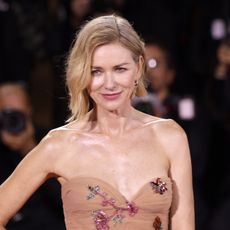 a white woman with short, blonde hair posing on a red carpet wearing a tan, strapless dress with sequins