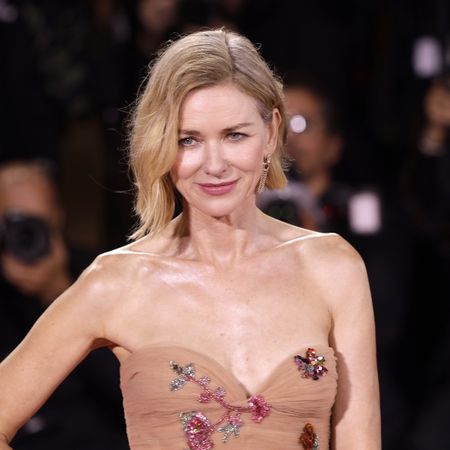 a white woman with short, blonde hair posing on a red carpet wearing a tan, strapless dress with sequins