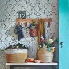 A hallway covered in a floral wallpaper with console table decorated with baskets filled with flowers