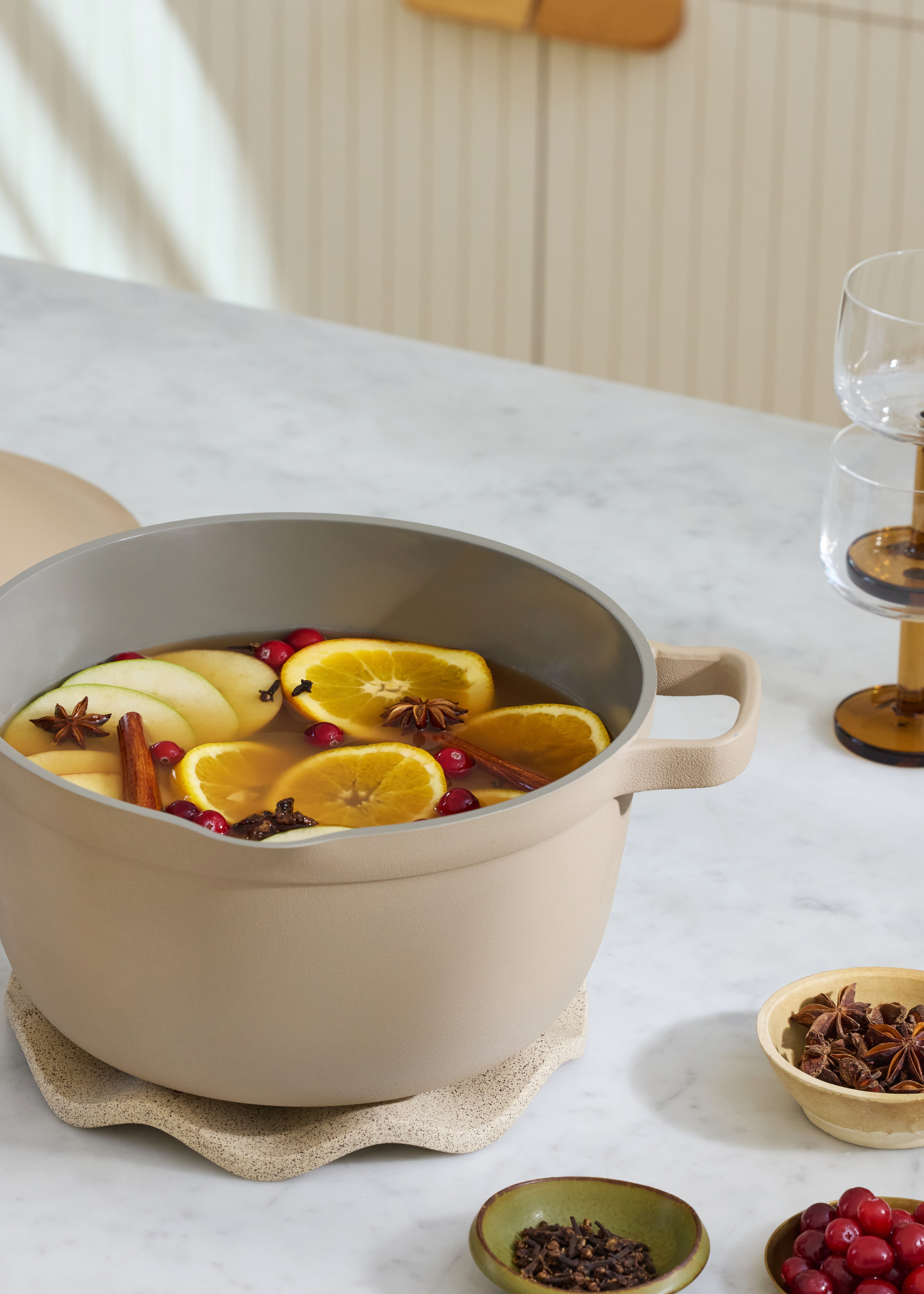 A ceramic simmer pot with berries, lemon slices, cloves, and cinnamon on a holder
