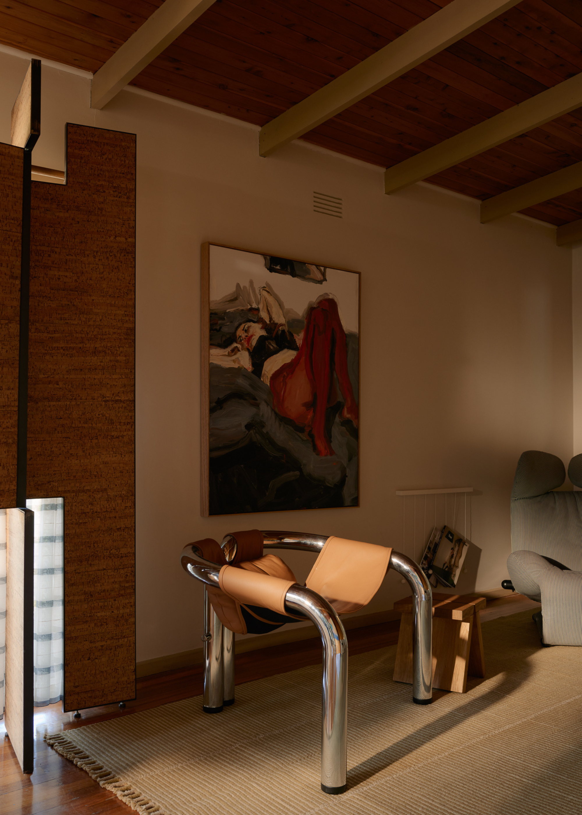A living room with framed wall art, a leather chrome chair, an area rug and sunlight streaming in