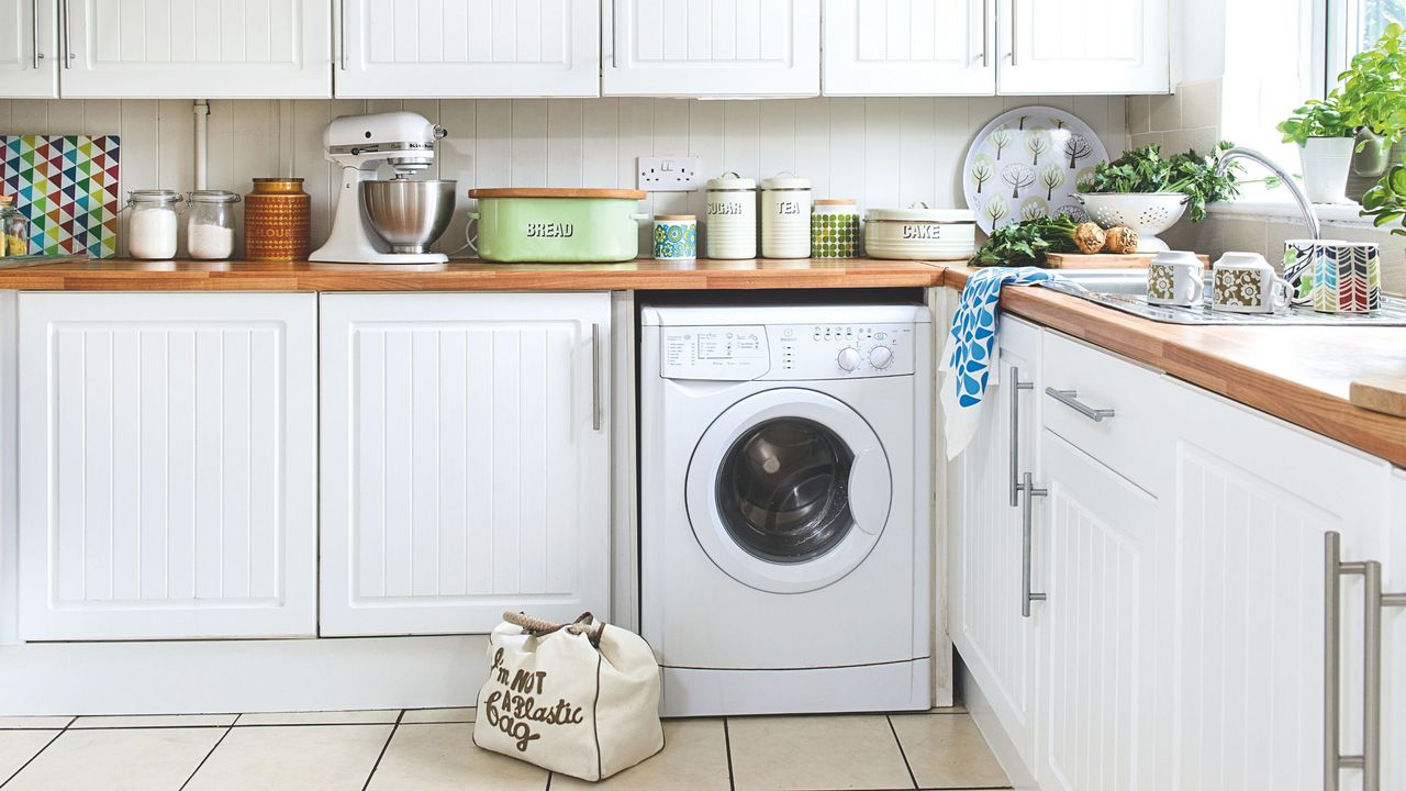 White washing machine in a white kitchen with wooden worktops and kitchen accessories on them