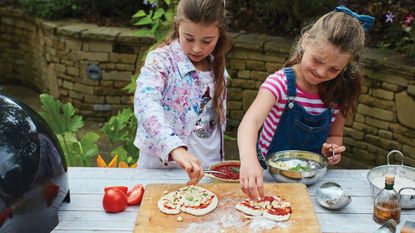 Kids preparing pizza outdoors at a toppings station