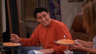 Matt LeBlanc as Joey Tribbiani smiles as he eats spaghetti.