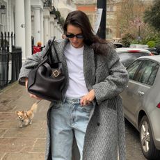 Fashion influencer Valeria in London wearing a chic fall outfit with faded baggy jeans, a white tee, long herringbone wool coat, and The Row's Margaux 17 black tote bag.