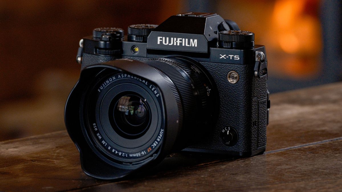 Fujifilm XF 16-50mm f/2.8-4.8 R LM WR lens mounted to a Fujifilm X-T5, in front of a wooden indoor background with a furnace