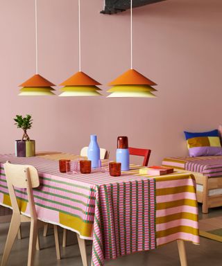colorful dining room with pink walls, patterned tablecloth and orange pendants