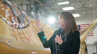 janet kavandi holding a microphone next to sierra space dram chaser under construction. far in the background is a u.s. flag