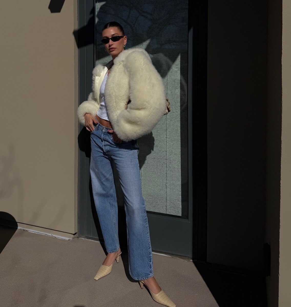 Hailey Bieber wearing a cream, fur jacket with vintage Levi's jeans and tan heels.