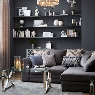 dark grey living room with wall-mounted shelves topped with accessories and décor and a grey sofa with patterned pillows and a modern coffee table