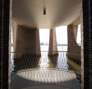 The ground floor of the Fjordenhus in Vejle, Denmark. A balcony with a metal railing overlooking brick archways in a lake.