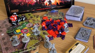 Components, board tiles, and models from Dragonlance: Warriors of Krynn lie on a wooden table in front of the board game box