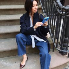 Woman in jeans and navy coat looking at her phone