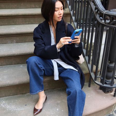 Woman in jeans and navy coat looking at her phone