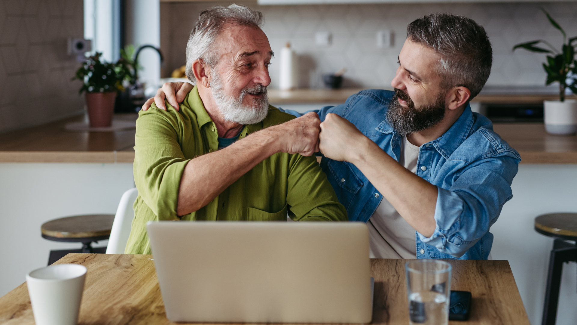 Older man and younger man fist bumping in front of a laptop