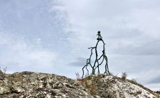 Sculpture of a woman walking on two large branches, on top of a hill