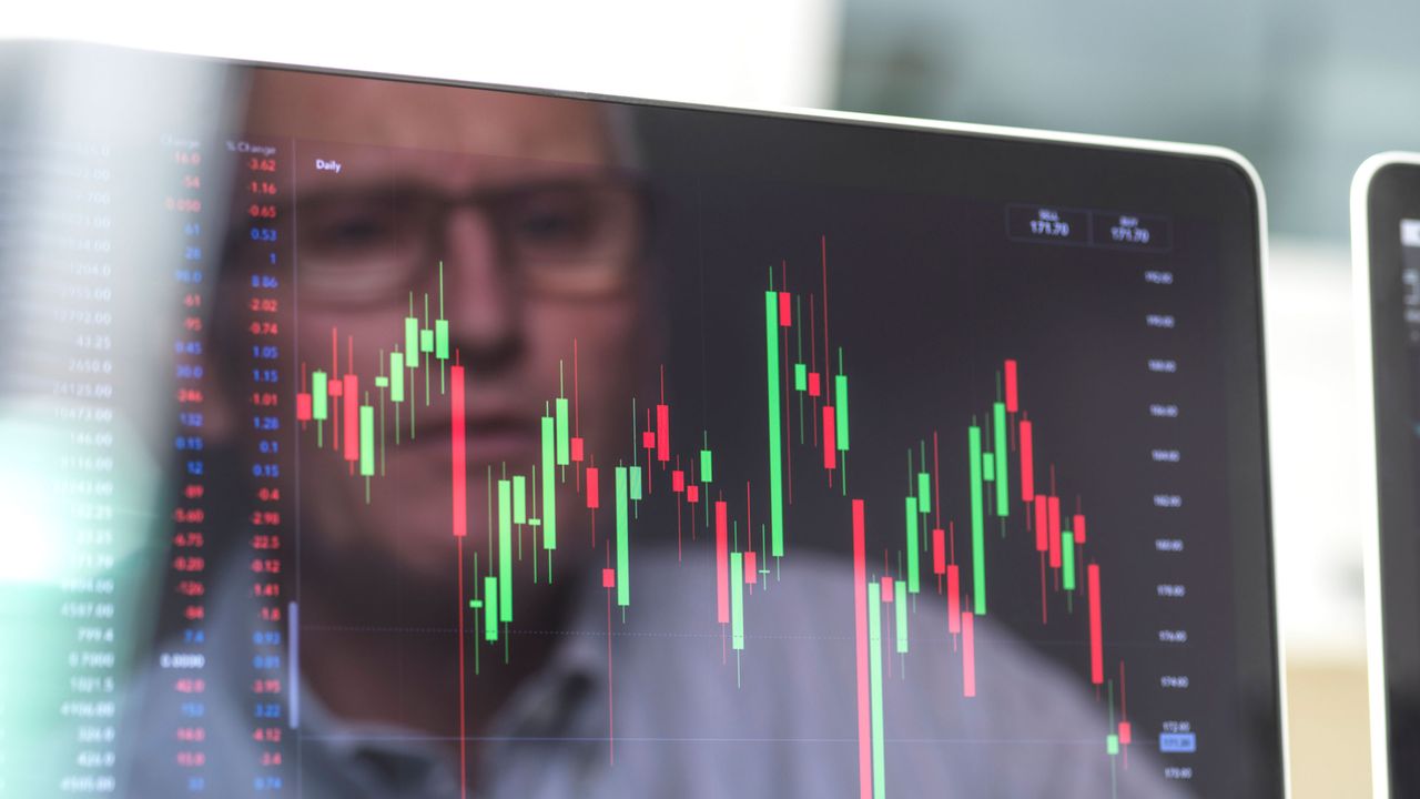 A man&amp;#039;s face is reflected in a computer screen showing volatile stock movement.