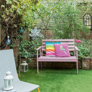Walled garden with artificial grass, pink bench with colourful cushions, lanterns and a plastic windmill