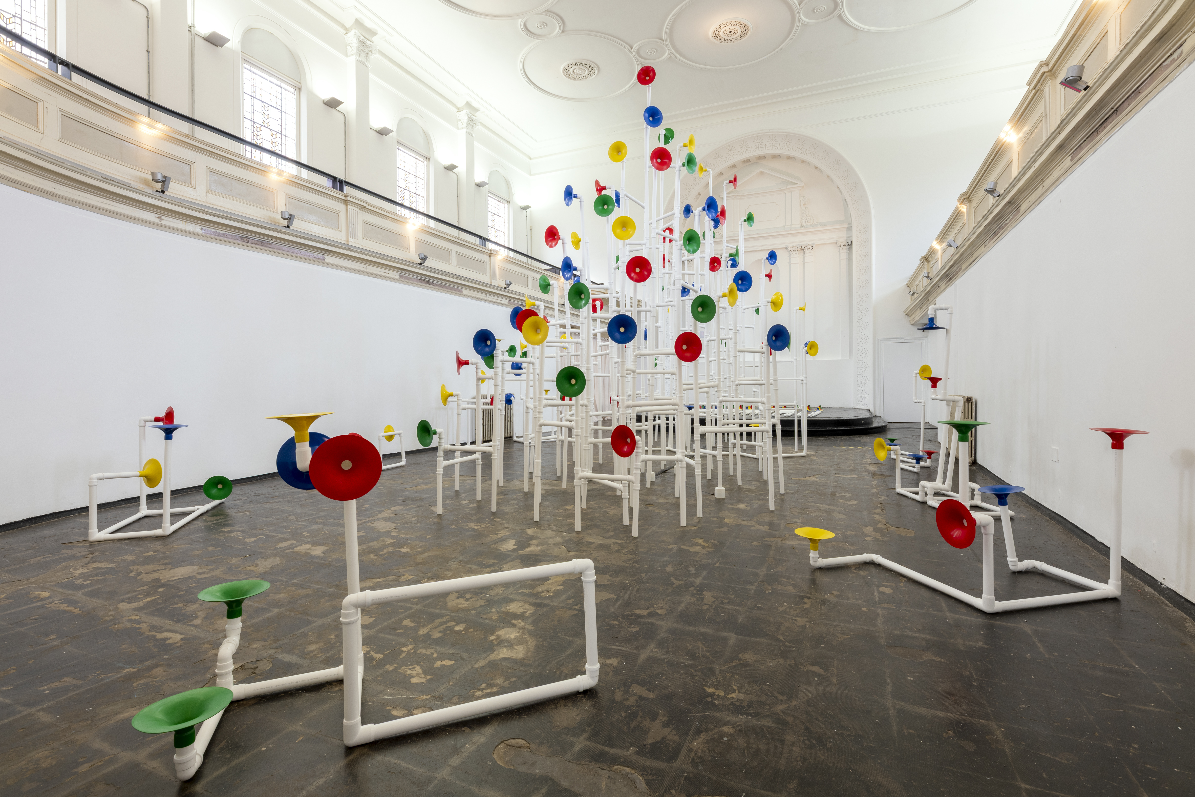 Installation in a former church made out of white pipes and colourful funnels