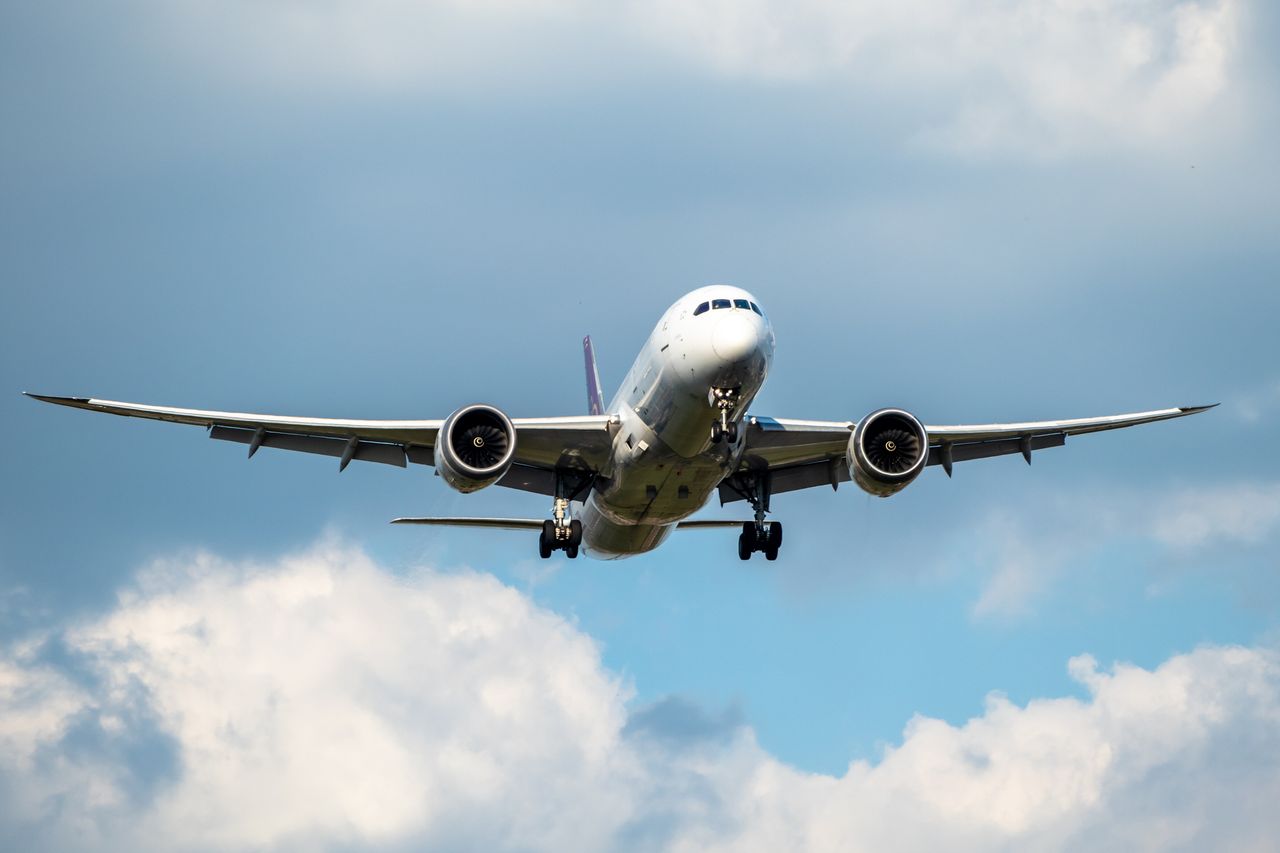 Front view of white 777 commercial flight airplane taking off or landing from the Airport runway with no visible markings or livery. Blue sky sunny back drop with some clouds