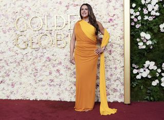 karla sofia gascon from emilia perez wears an orrange and yellow dress walking the red carpet at the 2025 golden globes