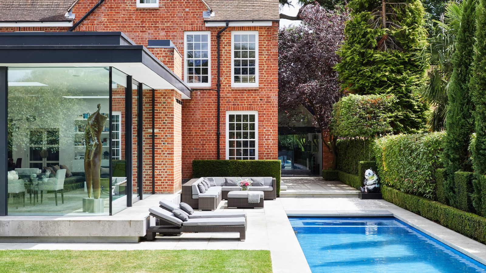 Exterior of house with dining room extension with glass wall, bespoke lap pool, a lawn and sun loungers