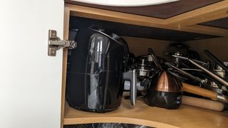 An air fryer stored in a cupboard with pans