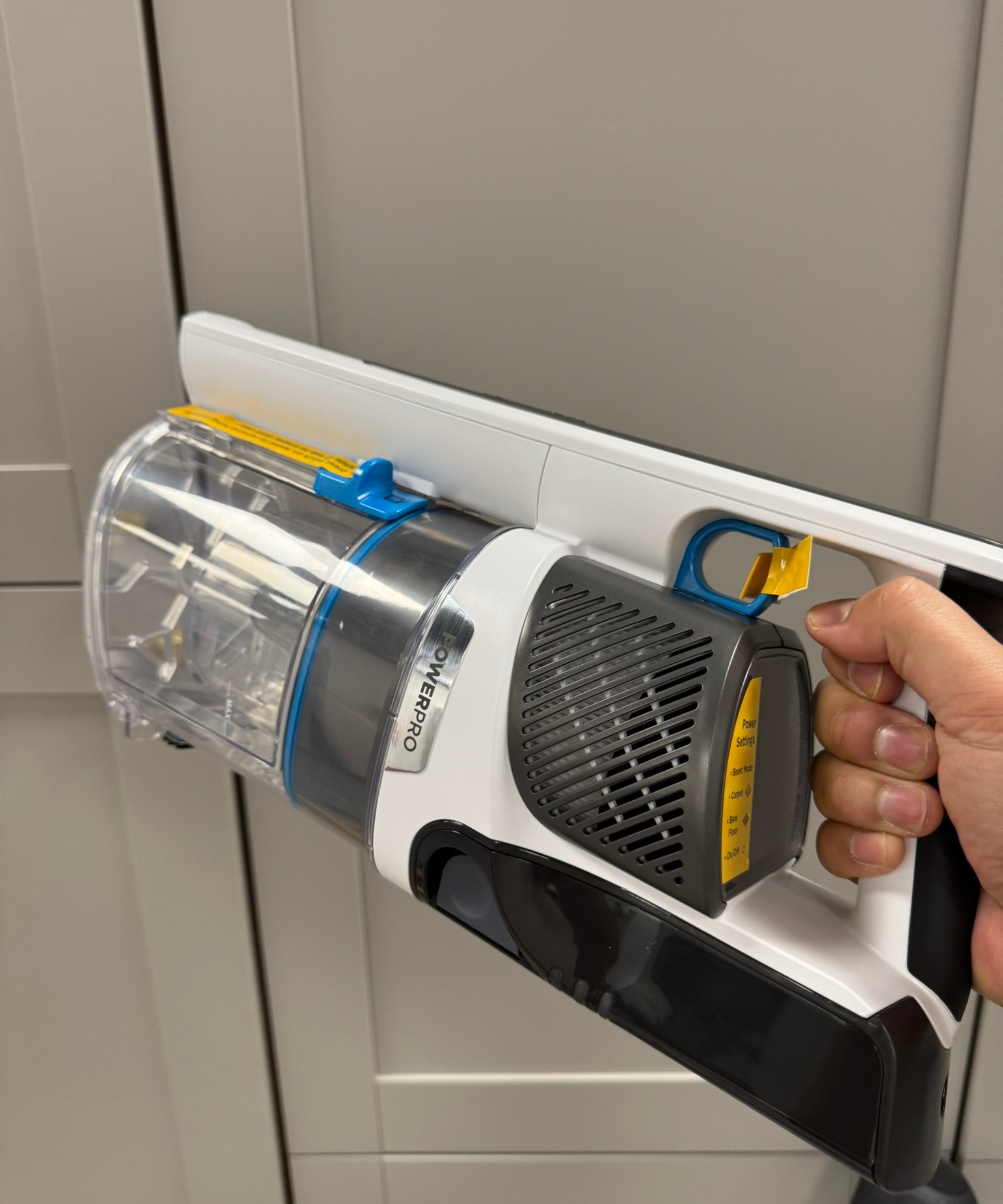 Hand holding the Shark PowerPro Pet cordless vacuum in front of gray cabinet doors.