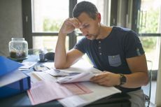 Man rests head on hand as he looks at financial document on desk.