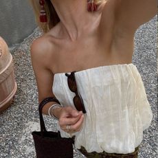 Woman wears cream pleated top, carries black woven leather handbag