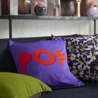 room with black sofa printed coloured cushions and flower in pot