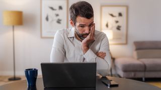 A man looking at his laptop in a stressed and upset manner