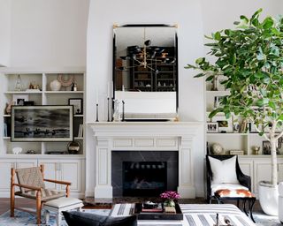 A family room with white walls, white fireplace, large mirror over the mantel, built-in shelves and brown and black armchairs