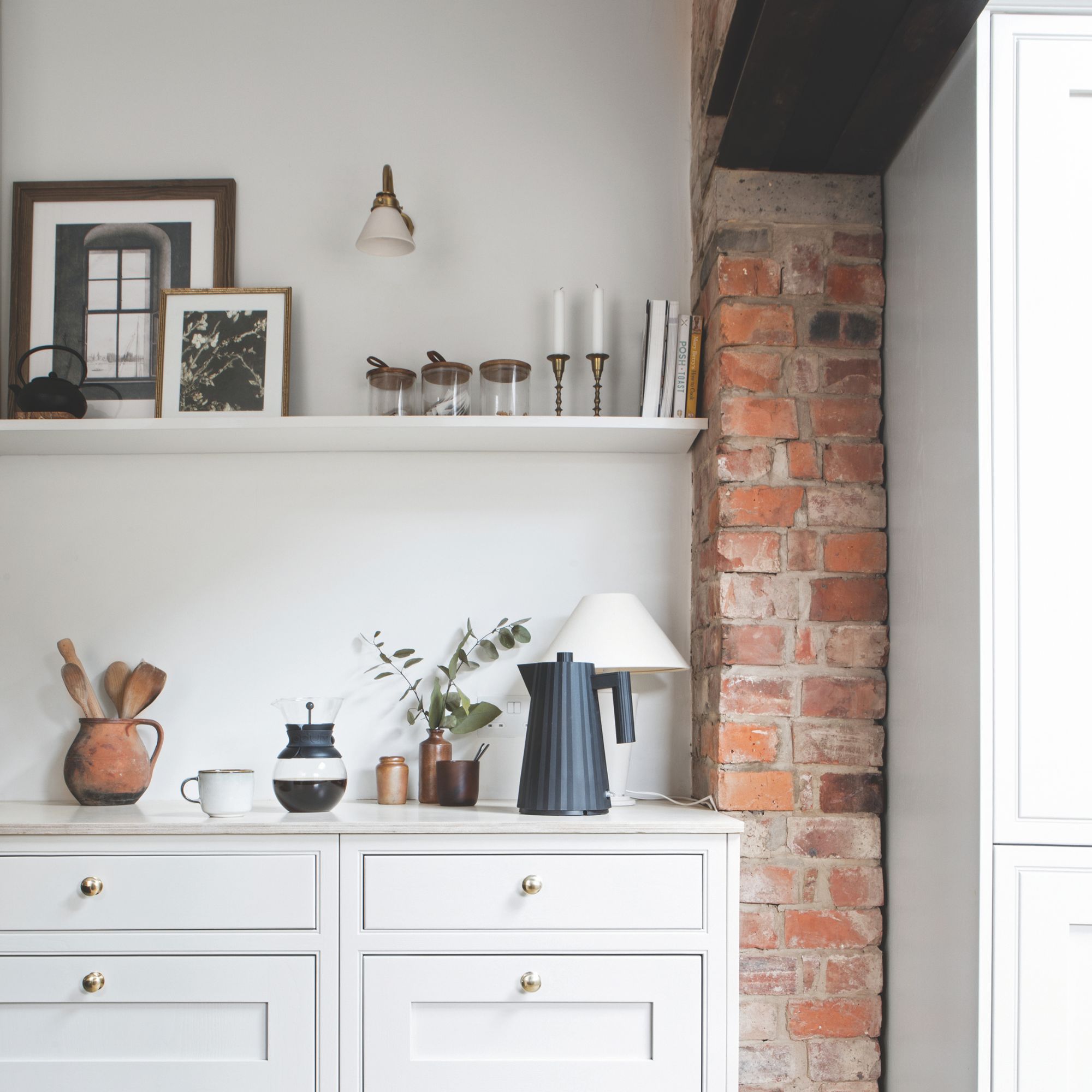 Light grey cabinet with a kettle and other trinkets on top, with a shelf above it