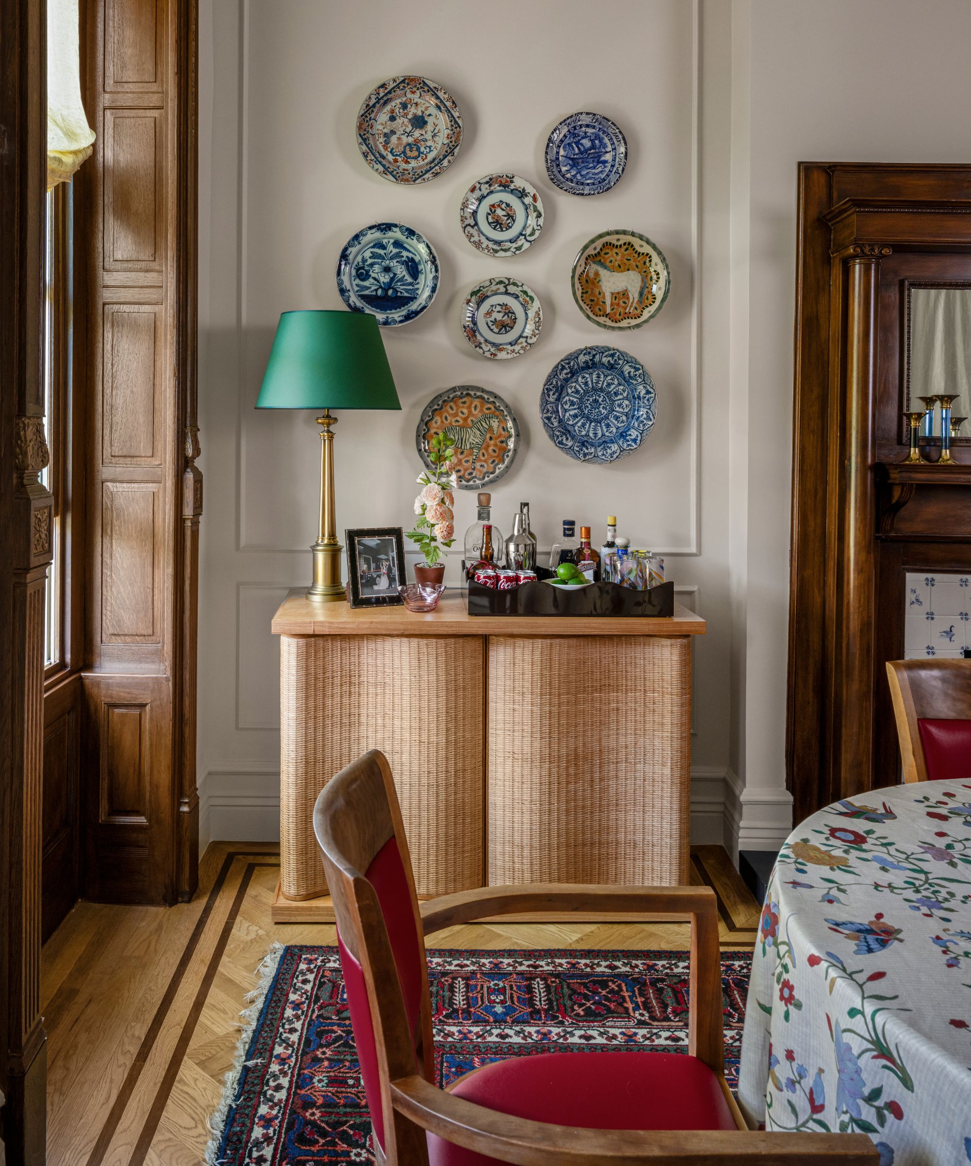 a neutral dining room in a historic brownstone with wooden fireplace, original windows, and a wicker console styled with antique plates