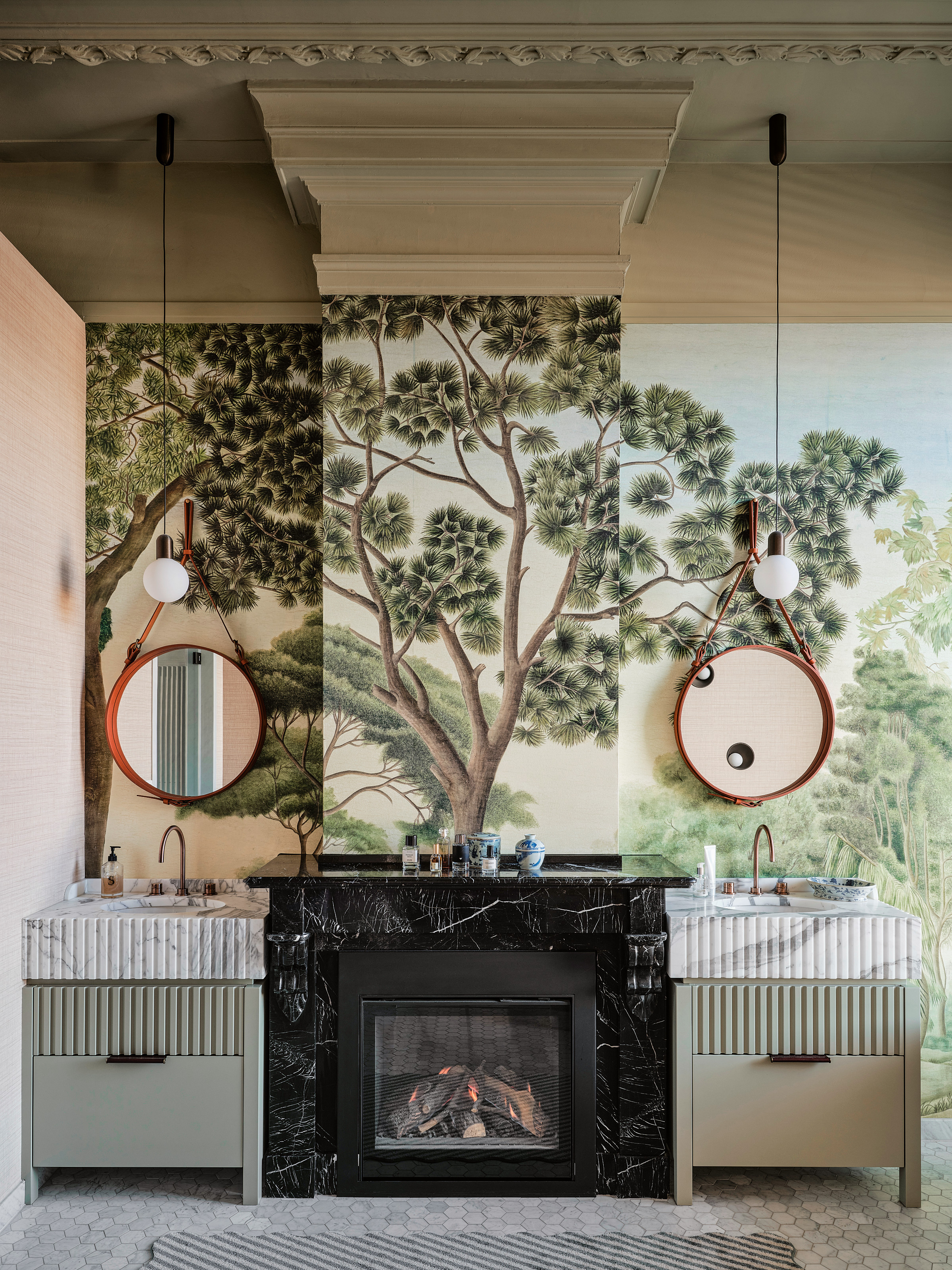 Bathroom with white and green double sink either side of a black stone fireplace, with tree mural behind
