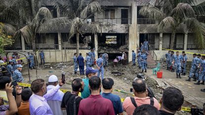 Onlookers gather as Bangladesh Air Force personnel inspect the crash site a day after a training jet crashed into a school in Dhaka